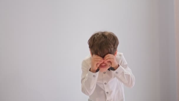 Sourire enfant garçon main cachant les yeux pour jeter un coup d'oeil amusant. Un beau gamin qui fait de beaux gestes comme des jumelles, des yeux qui regardent à travers les doigts. Expression folle. — Video