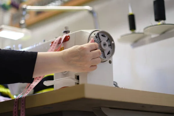 Female hands stitching white fabric on professional manufacturing machine at workplace. Close up view of sewing process. Light blurred background — Stock Photo, Image