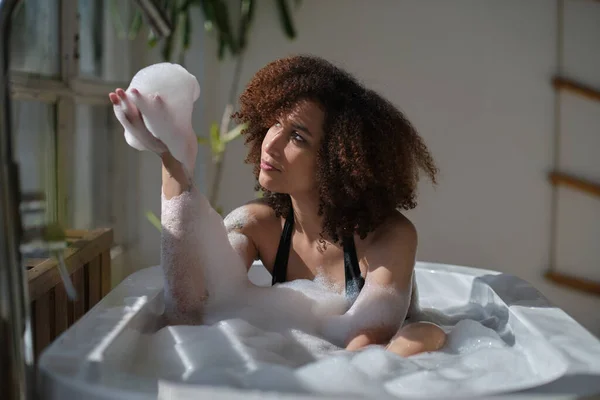 Sorrindo e relaxando afro-americana tomando banho em uma banheira cheia de espuma. Um tempo incrível. conceito de pessoas estilo de vida — Fotografia de Stock