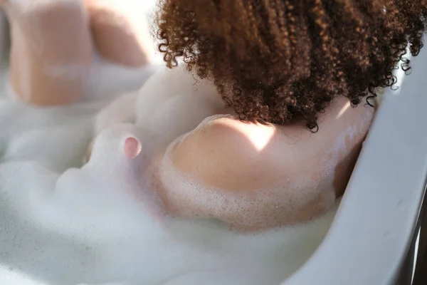 Улыбающаяся и расслабляющая африканская американка купается в ванне, полной пены. Удивительное время. образ жизни людей — стоковое фото