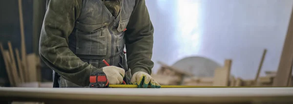 Close up. Carpenter holding a measure tape on the work bench. Woodwork and furniture making concept. Carpenter in the workshop marks out and assembles parts of the furniture cabinet — Stock Photo, Image