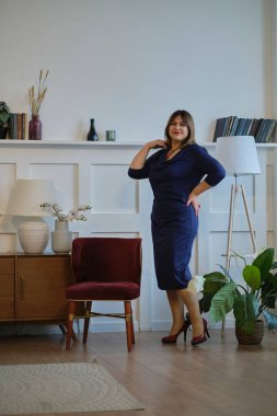 Evde abartılı giyinen bir bayan var. Kendine güvenen olgun bir kadının portresi. Gülümseyen kadın kameraya bakıyor. Başarılı orta yaşlı kadın gülümseyerek evde.