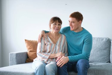 Kanepede, yetişkin oğlunun yanında oturan neşeli yaşlı kadın. Şefkatli oğul yaşlı annesine sarılır. Farklı nesiller arasındaki ilişkiler.