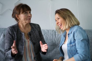Yetişkin kızı yaşlı annesiyle konuşuyor. Anne ve kızı sohbetten zevk alıyorlar modern oturma odasındaki koltukta oturuyorlar. veli ilişkisi kavramı