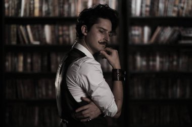 Karanlık bir kütüphane odasında düşünceli bir adam gece ayakta duruyor. Bıyıklı şık bir adam bileziği düzeltiyor..