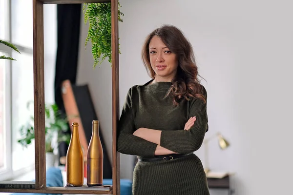 Smiling woman standing with her arms crossed and looking at camera. She is standing in a modern apartments