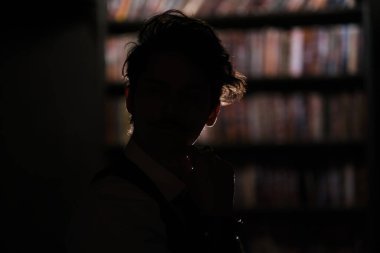 Şık giyinmiş bir adam pencerede durur ve mesafeye bakar. Düşünceli adam gece karanlık bir odada duruyor.