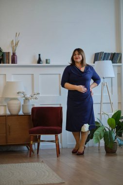 Evde abartılı giyinen bir bayan var. Kendine güvenen olgun bir kadının portresi. Gülümseyen kadın kameraya bakıyor. Başarılı orta yaşlı kadın gülümseyerek evde.