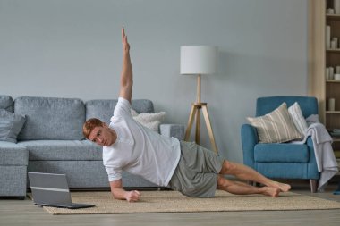 Self-care during stay at home. Fitness training, stretching exercises online men at home with laptop. guy lying on fitness mat online yoga lessons blank laptop screen clipart