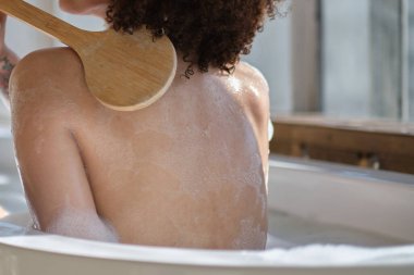 Gülümseyen ve rahatlatan Afro-Amerikan kadın köpük dolu bir küvette banyo yapıyor. Harika bir zaman. Yaşam tarzı insan kavramı