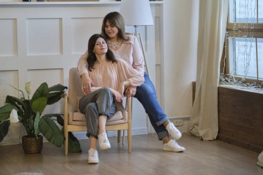 Güzel son sınıf annesi ve yetişkin kızı evde kanepede otururken sarılıp gülümsüyorlar.