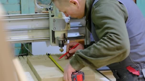 Κλείσε. Ο ξυλουργός κρατάει μια μεζούρα στον πάγκο εργασίας. Ξυλουργικές εργασίες και έπιπλα κάνοντας έννοια. Ξυλουργός στο εργαστήριο επισημαίνει και συναρμολογεί μέρη του ντουλαπιού επίπλων — Αρχείο Βίντεο
