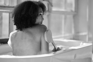 Gülümseyen ve rahatlatan Afro-Amerikan kadın köpük dolu bir küvette banyo yapıyor. Harika bir zaman. Yaşam tarzı insan kavramı