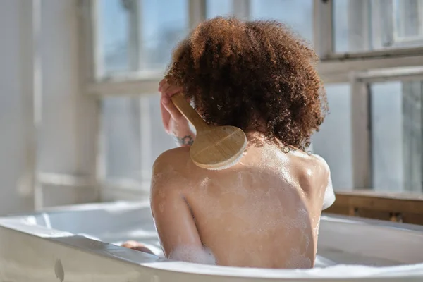 Femme afro-américaine souriante et relaxante se baignant dans une baignoire pleine de mousse. Un temps incroyable. style de vie gens concept — Photo