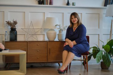 Evde abartılı giyinen bir bayan var. Kendine güvenen olgun bir kadının portresi. Gülümseyen kadın kameraya bakıyor. Başarılı orta yaşlı kadın gülümseyerek evde.