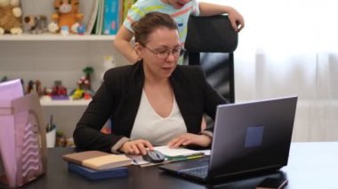 Serbest çalışan bir anne, çocuğu evde oynarken bilgisayarını uzaktan çalıştırmaya çalışıyor. Evden işe giden aile..