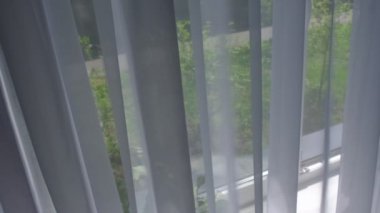 Odadaki açık pencereden rüzgar esiyor. Pencerenin yanında beyaz tül sallıyor.