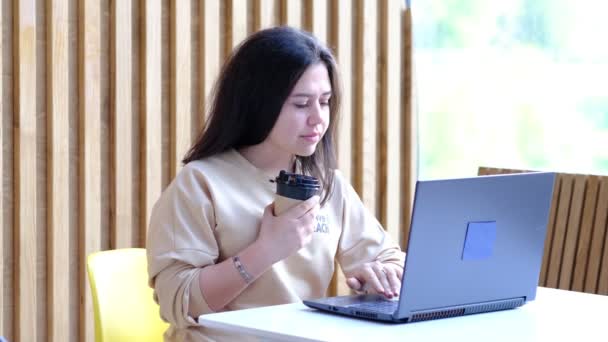 Mulher jovem hipster sentado no café, beber café e usando laptop.On mesa é laptop. Menina navegando na internet, conversando, blogging. — Vídeo de Stock