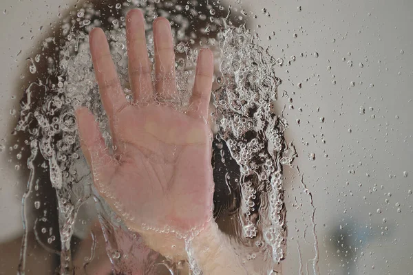 Female hand on the glass door of the shower stall. Sensual portrait of young woman taking a shower. Defocused female looks through the glass of the shower stall. — Stock Photo, Image