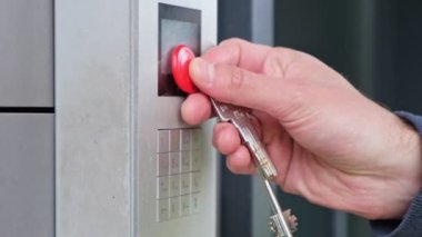 Erkek, bina girişinde dahili telefon kullanıyor. Elektronik kod kilidini açar. Man Hand güvenlik sistemi kodunu giriyor, işaret parmağı dahili iletişim cihazı giriş kapısı olan düğmeye basıyor.
