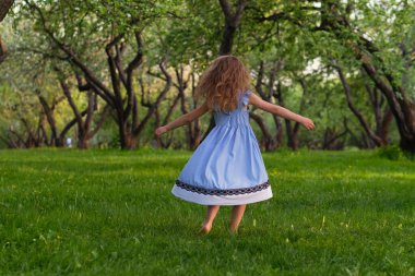 Küçük kız çimenlerde yalınayak koşuyor. Sıcak bir yaz gününde mutlu bir çocuk..