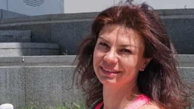 Kadın yana bakıyor, yüzünü kameraya çeviriyor ve güneşli yaz gününde açık havada gülümsüyor. Sokakta mutlu bir kadın. Kapat.