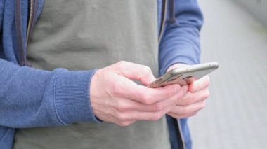 Yakından çekim yapan adam şehir caddesindeki cep telefonundan mesaj yazıyor. Genç erkek telefonda ağır çekimde sohbet ediyor..