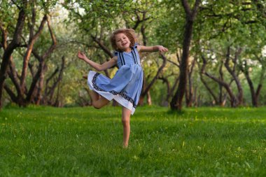 Küçük kız çimenlerde yalınayak koşuyor. Sıcak bir yaz gününde mutlu bir çocuk..