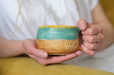 Beyaz elbiseli tanınmayan bir kadın sarı bir koltukta oturuyor ve elinde sarı bir bardak tutuyor..