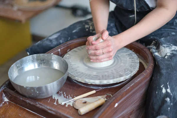 Τα κλειστά γυναικεία χέρια φτιάχνουν πιάτα από πηλό. τα χέρια των γυναικών που δουλεύουν σε τροχό αγγειοπλαστών. Ο κύριος αγγειοπλάστης εργάζεται σε εργαστήριο — Φωτογραφία Αρχείου