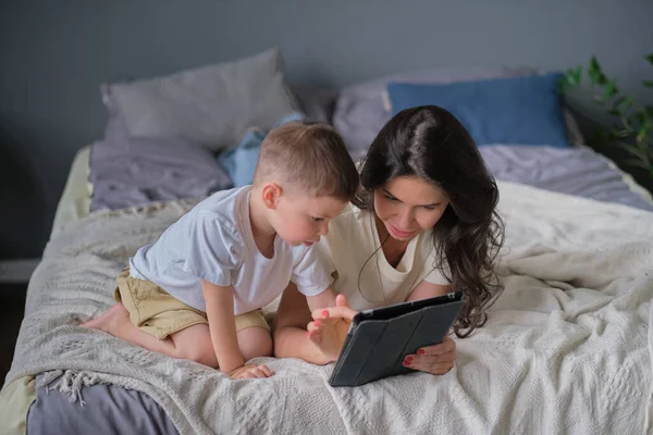 Anya és fia tablettel otthon. Anya mutatja média tartalom on-line a fiának egy tabletta a nappaliban egy ház belsejében — Stock Fotó