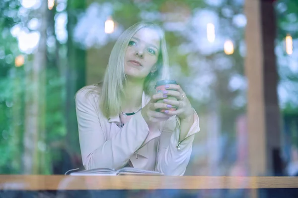 Женщина в кафе сидит за столом, пьет кофе и смотрит в сторону. винтажный тон — стоковое фото