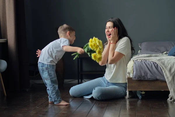 Grattis på mors dag. barn son gratulerar mor på semester och ger blommor. Grattis till mödradagen under semestern hemma — Stockfoto