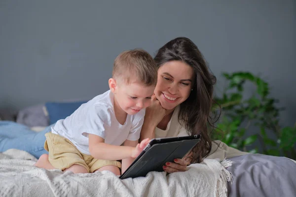 Mother and son with tablet at home. Mother showing media content on line to her son in a tablet in the living room in a house interior — Stock Photo, Image