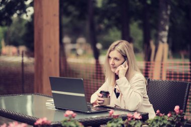 Kafedeki masada oturan iş kadını, cep telefonuyla konuşan ve not defterine not alan. Masada dizüstü bilgisayar ve bir fincan kahve var. Öğrenci çevrimiçi öğreniyor. Çevrimiçi çalışan serbest yazar.
