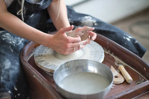 Τα κλειστά γυναικεία χέρια φτιάχνουν πιάτα από πηλό. τα χέρια των γυναικών που δουλεύουν σε τροχό αγγειοπλαστών. Ο κύριος αγγειοπλάστης εργάζεται σε εργαστήριο — Φωτογραφία Αρχείου