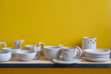 Seramik çömlek atölyesinin bir parçası olarak raflardaki bitmemiş kil kaplar. Yaratıcı stüdyo çömlekçisi. Ahşap raflarda farklı seramik bulaşık takımı.