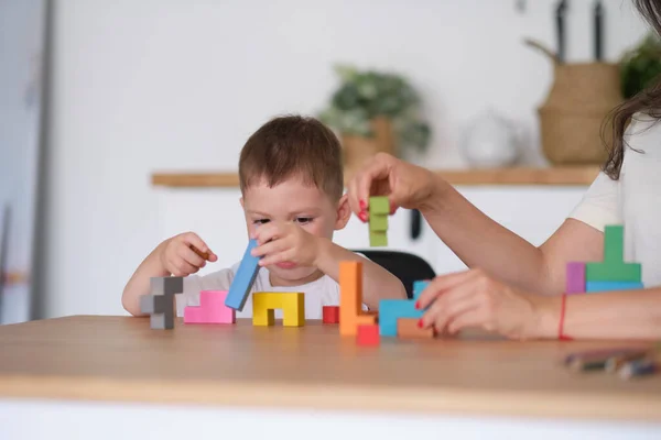 子供の男の子と母親が家のテーブルでおもちゃを遊んでいます。テーブルの上でカラフルな木製のレンガで遊ぶ子供たちは. — ストック写真