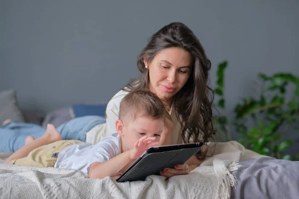 Anya és fia tablettel otthon. Anya mutatja média tartalom on-line a fiának egy tabletta a nappaliban egy ház belsejében — Stock Fotó