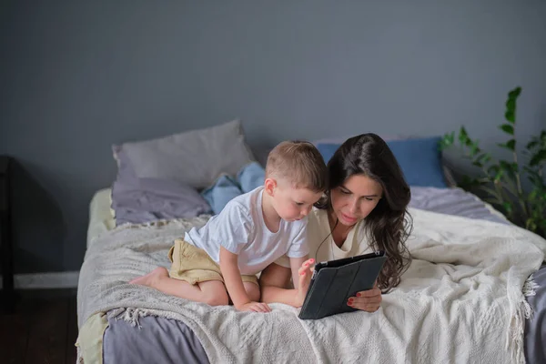 Mother and son with tablet at home. Mother showing media content on line to her son in a tablet in the living room in a house interior — Stock Photo, Image