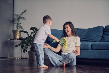 Anneler Günün kutlu olsun. Çocuk evlat tatilde annesini tebrik eder ve çiçek verir. Evde bayram kutlamaları sırasında anneler günü için onu tebrik etmek.