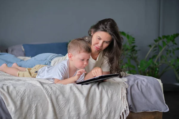 mother and son with tablet at home. Mother showing media content on line to her son in a tablet in the living room in a house interior