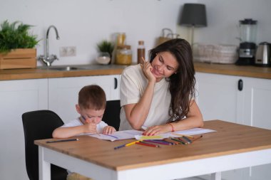 Küçük çocuk resim yapmayı öğreniyor. Anne ve oğlu kalemlerle çizim yaparken eğleniyor. Çocukların yaratıcılığı.