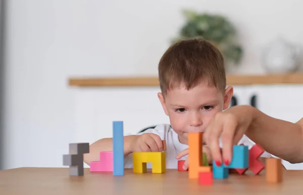 子供の男の子と母親が家のテーブルでおもちゃを遊んでいます。テーブルの上でカラフルな木製のレンガで遊ぶ子供たちは. — ストック写真