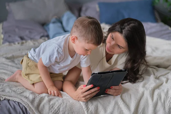 Mother and son with tablet at home. Mother showing media content on line to her son in a tablet in the living room in a house interior — Stock Photo, Image