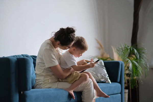 Anya és fia tablettel otthon. Anya mutatja média tartalom on-line a fia egy tabletta ül egy kanapén a nappaliban egy házban belső — Stock Fotó