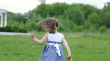 Tarlada koşan küçük kız. Kız sadece arkadan görülebilir. Kız etrafına bakıyor. Parktaki mutlu çocuk rüyanın tadını çıkarıyor. Mutlu olmak için çocuk arzusu.