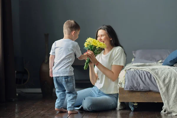 Šťastný den matek. syn blahopřeje matce k dovolené a dává květiny. blahopřát jí na Den matek během svátků oslavy doma — Stock fotografie