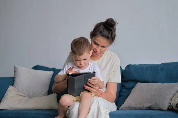 Mother and son with tablet at home. Mother showing media content on line to her son in a tablet sitting on a couch in the living room in a house interior — Stock Photo, Image
