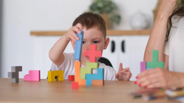 Pojke och mor leker pedagogiska leksaker hemma. barn leker med färgglada träklossar vid bordet. — Stockfoto